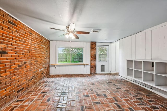 unfurnished room with brick floor, visible vents, brick wall, and a ceiling fan