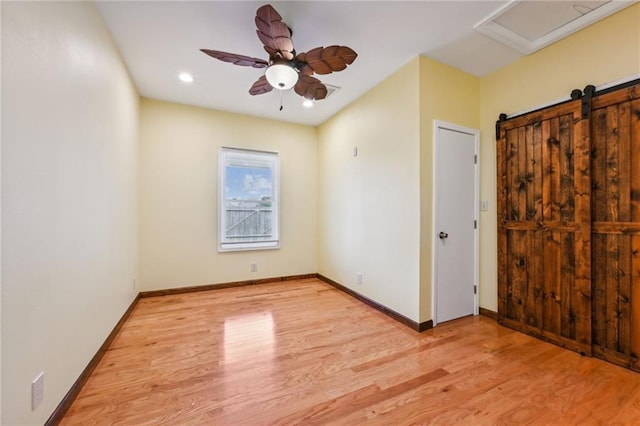 unfurnished bedroom with recessed lighting, light wood-style flooring, a barn door, a ceiling fan, and baseboards