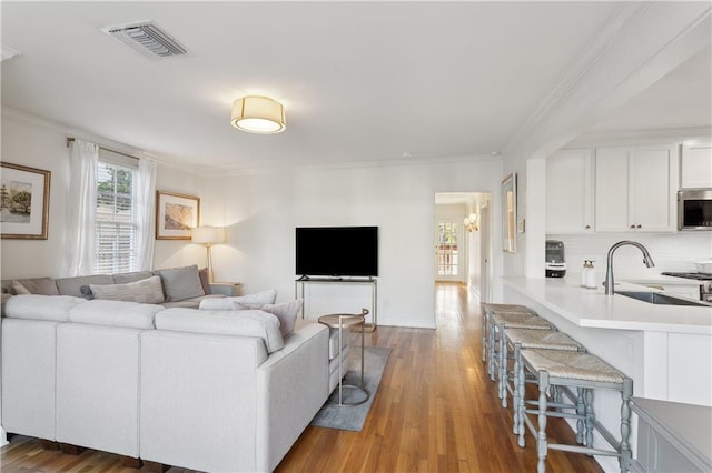 living room featuring sink, ornamental molding, and light hardwood / wood-style floors