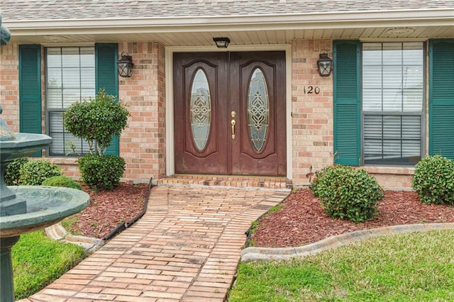 doorway to property featuring brick siding and a shingled roof