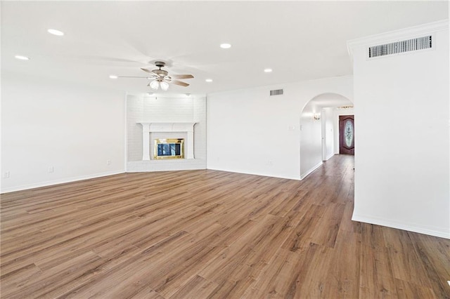 unfurnished living room with visible vents, wood finished floors, a brick fireplace, and ceiling fan