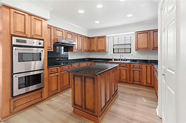 kitchen with under cabinet range hood, double oven, brown cabinetry, and a sink