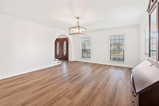 unfurnished dining area with arched walkways, light wood-type flooring, a wealth of natural light, and ornamental molding