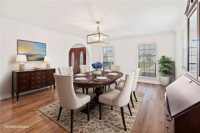 dining space featuring a notable chandelier, wood finished floors, arched walkways, and ornamental molding