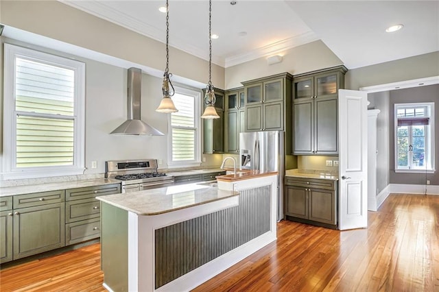 kitchen featuring an island with sink, stainless steel appliances, hanging light fixtures, sink, and wall chimney range hood