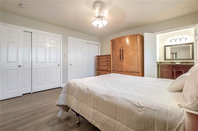 bedroom featuring hardwood / wood-style flooring, two closets, ensuite bath, and ceiling fan