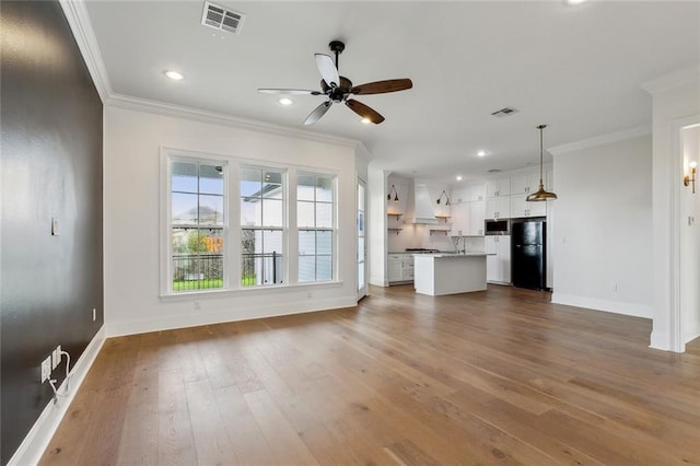 unfurnished living room with visible vents, wood finished floors, and ornamental molding