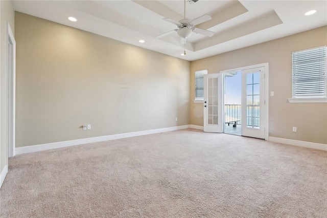 carpeted empty room with ceiling fan, a raised ceiling, and french doors