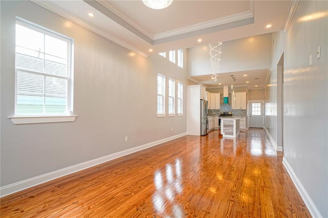 unfurnished living room with an inviting chandelier, light hardwood / wood-style floors, a wealth of natural light, and crown molding