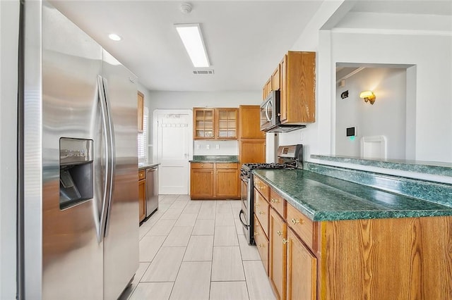 kitchen featuring brown cabinets, dark countertops, visible vents, appliances with stainless steel finishes, and glass insert cabinets