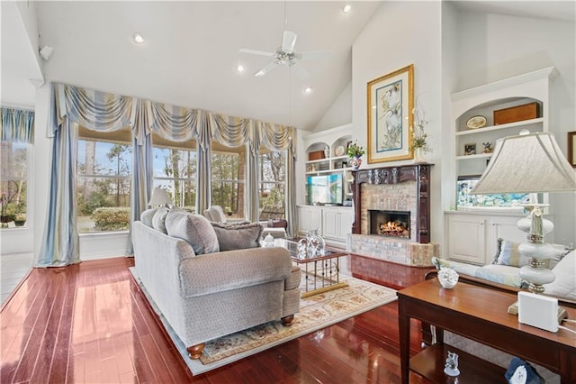 living room with high vaulted ceiling, ceiling fan, hardwood / wood-style floors, a fireplace, and built in features