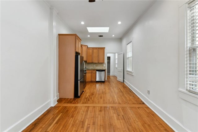 kitchen with backsplash, a skylight, stainless steel appliances, and light hardwood / wood-style floors