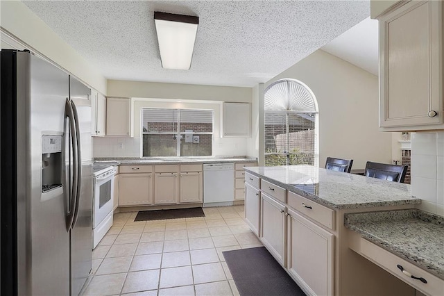 kitchen featuring white appliances, light stone counters, light tile patterned flooring, a breakfast bar area, and tasteful backsplash