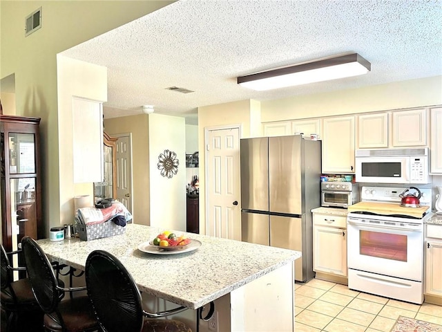 kitchen with white appliances, a peninsula, light tile patterned floors, a textured ceiling, and light stone countertops