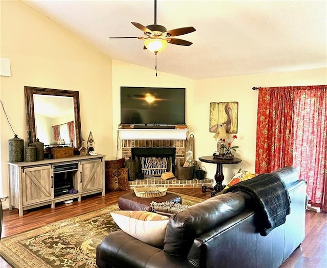 living room with vaulted ceiling, a ceiling fan, dark wood-type flooring, and a brick fireplace