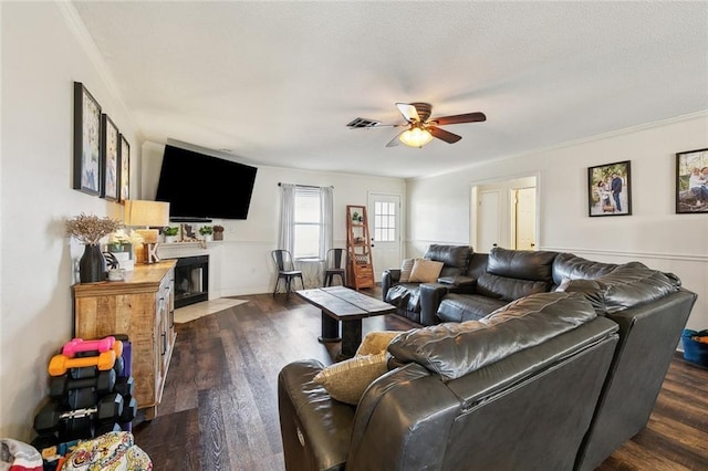 living room with visible vents, a fireplace with flush hearth, a ceiling fan, and dark wood-style flooring