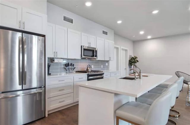 kitchen with sink, white cabinetry, stainless steel appliances, a kitchen island with sink, and tasteful backsplash