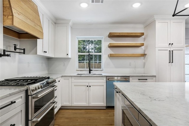 kitchen with appliances with stainless steel finishes, sink, premium range hood, white cabinetry, and light stone countertops