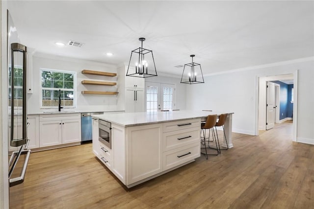 kitchen with white cabinetry, stainless steel appliances, a center island, decorative light fixtures, and sink