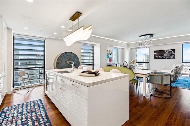 kitchen with white cabinets, an island with sink, a sink, decorative light fixtures, and dark wood-style flooring