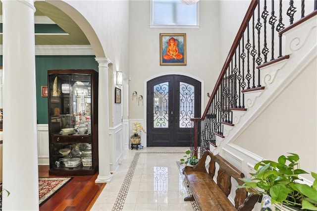 foyer featuring ornamental molding, french doors, ornate columns, and a towering ceiling