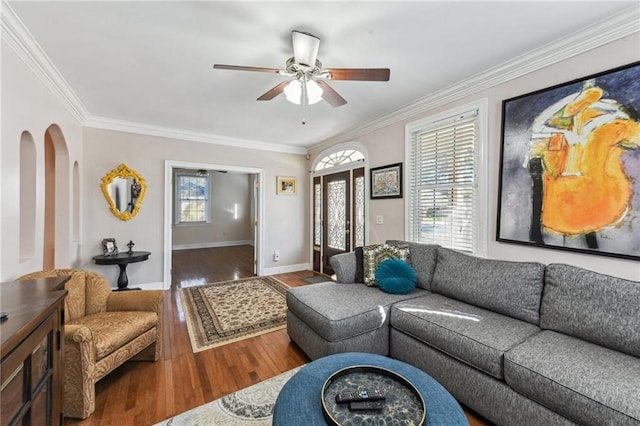 living room with arched walkways, ornamental molding, ceiling fan, wood finished floors, and baseboards