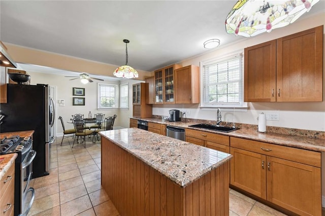 kitchen with brown cabinetry, glass insert cabinets, appliances with stainless steel finishes, a center island, and a sink