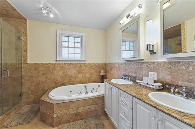 bathroom with double vanity, a tub with jets, a stall shower, and a sink