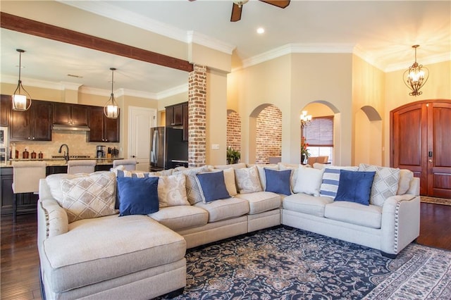 living room with ceiling fan with notable chandelier, crown molding, dark wood-type flooring, and sink