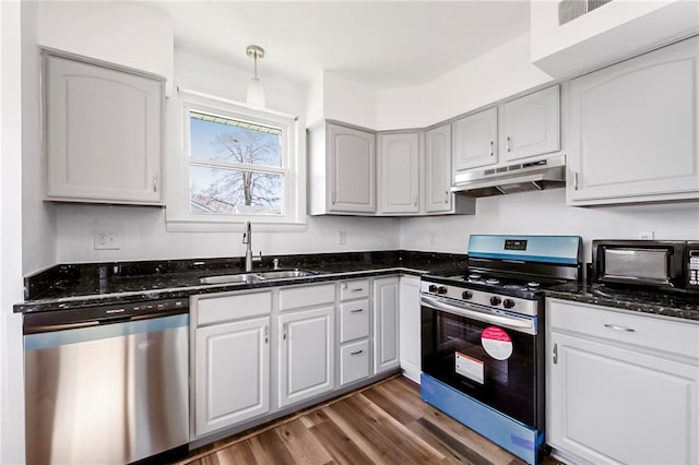 kitchen with appliances with stainless steel finishes, sink, dark stone counters, and dark hardwood / wood-style floors