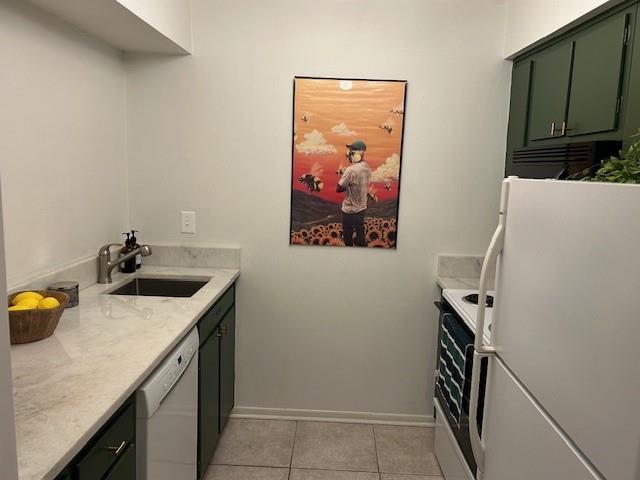 kitchen with white appliances, light tile patterned floors, baseboards, green cabinets, and a sink