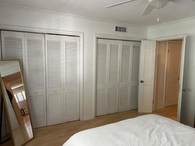 bedroom with light wood-type flooring, ceiling fan, visible vents, and multiple closets