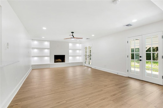 unfurnished living room with visible vents, light wood-style flooring, ceiling fan, french doors, and a fireplace