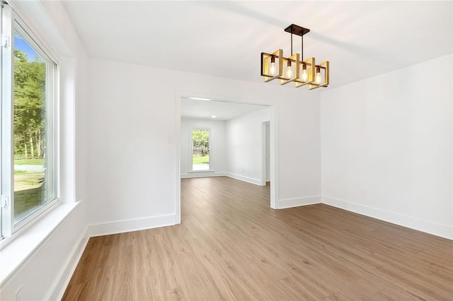 empty room featuring light wood-type flooring, a notable chandelier, and baseboards