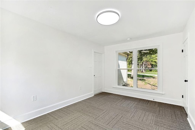 unfurnished room with dark carpet and baseboards