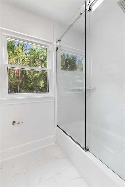 bathroom with marble finish floor, bath / shower combo with glass door, and baseboards