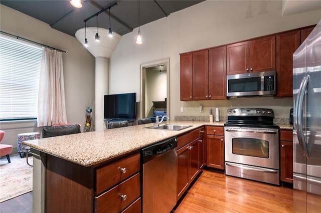 kitchen featuring hanging light fixtures, stainless steel appliances, light hardwood / wood-style floors, sink, and kitchen peninsula