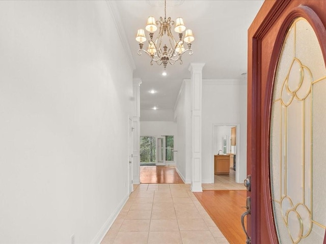 hall featuring light wood-type flooring, an inviting chandelier, crown molding, and decorative columns