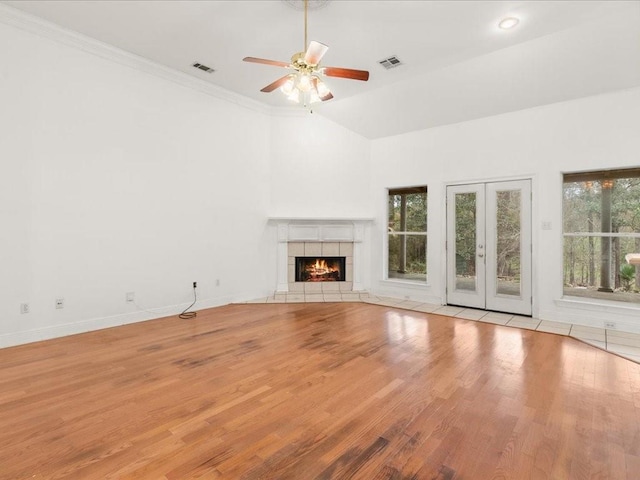 unfurnished living room with french doors, light hardwood / wood-style flooring, a tile fireplace, ceiling fan, and crown molding