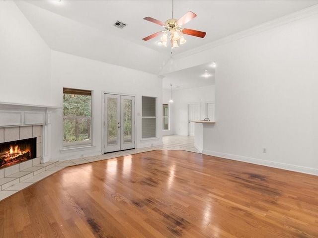 unfurnished living room featuring light hardwood / wood-style floors, crown molding, ceiling fan, a fireplace, and french doors