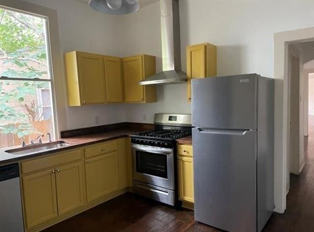 kitchen featuring appliances with stainless steel finishes, dark wood-style flooring, a sink, and wall chimney range hood