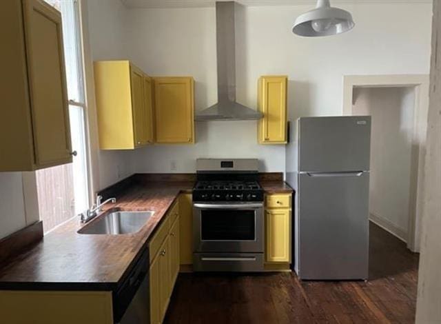 kitchen featuring dark wood finished floors, dark countertops, appliances with stainless steel finishes, a sink, and wall chimney exhaust hood