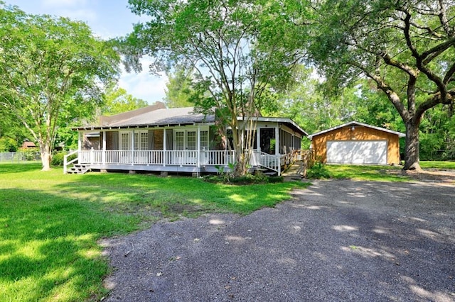 view of front of house with covered porch, a front yard, a garage, and an outbuilding