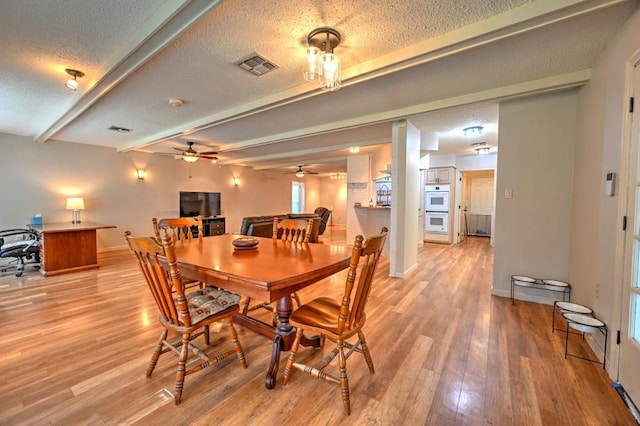 dining room featuring a textured ceiling, ceiling fan, beamed ceiling, and light hardwood / wood-style floors