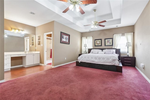 bedroom with built in desk, ensuite bath, a raised ceiling, carpet floors, and sink