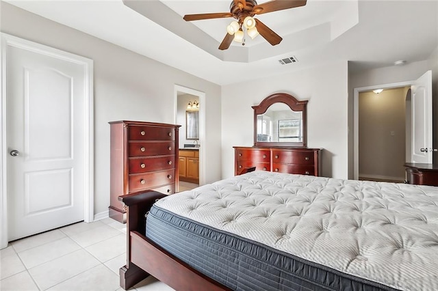 bedroom with ensuite bath, light tile patterned floors, ceiling fan, and a raised ceiling