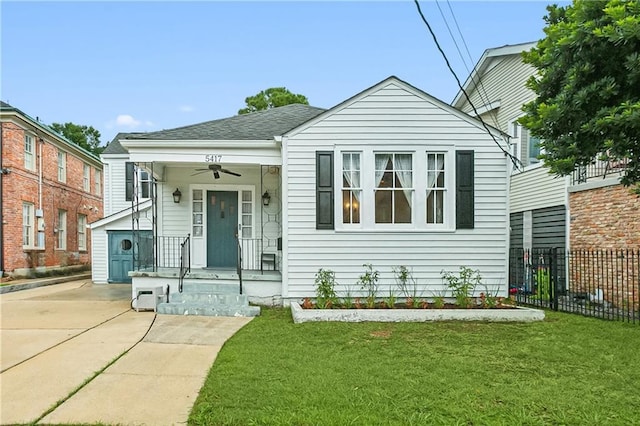 bungalow-style home with roof with shingles, fence, a front lawn, and a ceiling fan