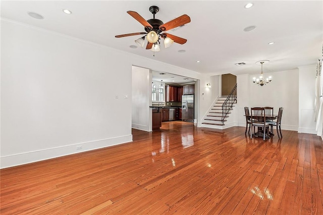 unfurnished living room with ceiling fan with notable chandelier, stairway, baseboards, and wood finished floors