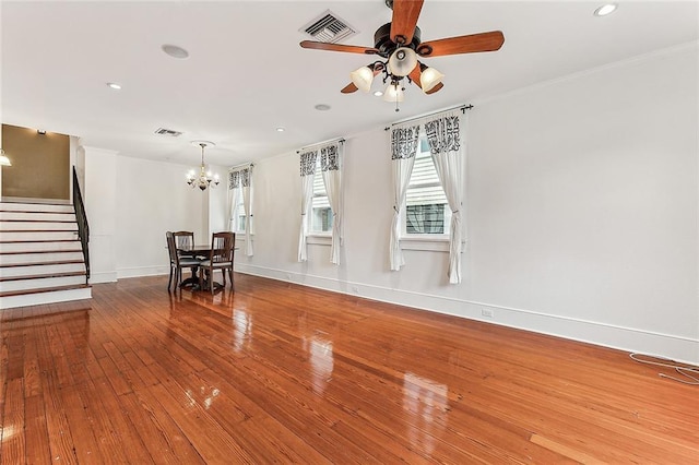 unfurnished living room with stairs, ceiling fan with notable chandelier, wood finished floors, and visible vents