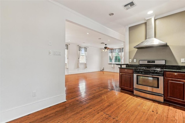 kitchen with wall chimney range hood, stainless steel gas stove, visible vents, light wood finished floors, and open floor plan